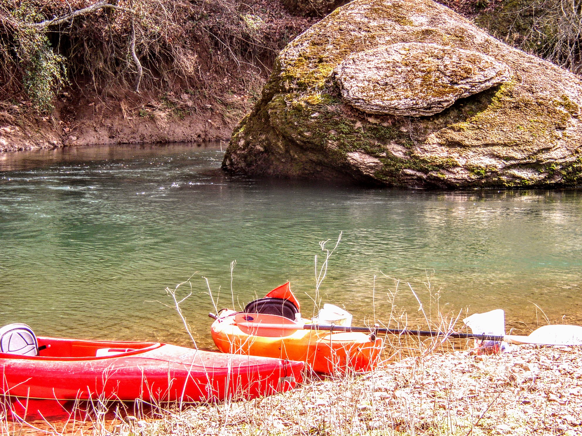 Two kayaks on the bank next to a large worn bluff rock